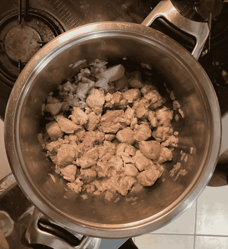 Fazékban piruló kockázott sertéshús és finomra vágott vöröshagyma a lencsegulyás alapjához.